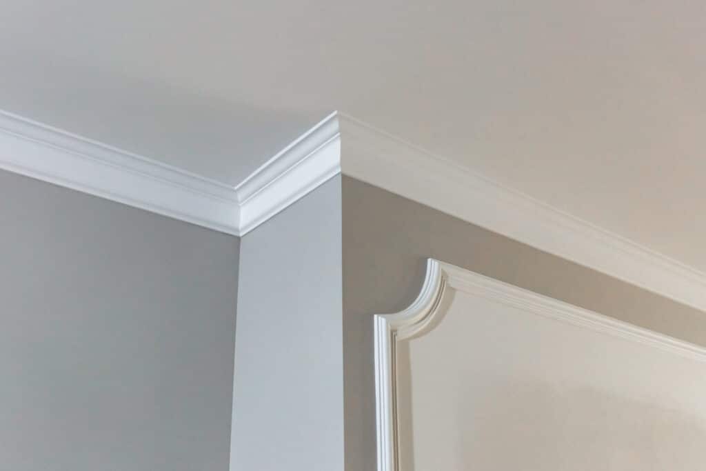 Angle de pièce moderne avec murs gris et plafond blanc. Corniche et moulure décorative murales blanches élégantes, design intérieur.