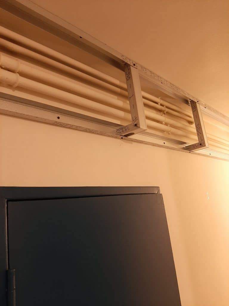 Cadre métallique NACEP supportant des conduits blancs parallèles sous un plafond. Une armoire sombre légèrement ouverte est visible en bas.