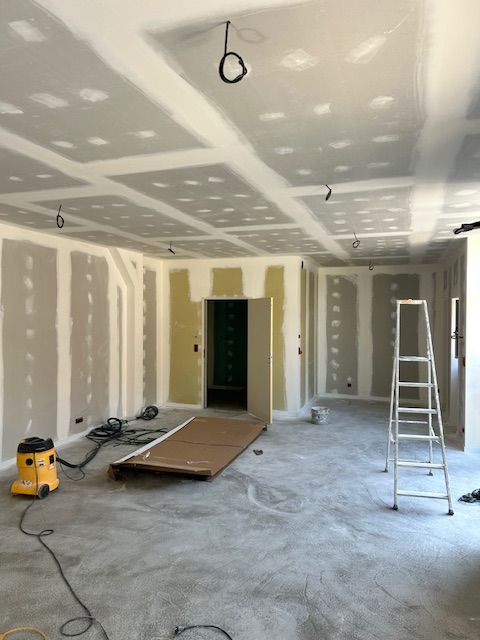 Pièce en chantier avec murs et plafond en placo-plâtre jointoyé, fils électriques pendants. Aspirateur de chantier et échelle présents sur le sol en béton.