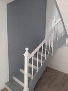 Escalier bicolore gris et blanc, balustrade immaculée, murs gris-bleu et sol parquet clair, pour un intérieur moderne.