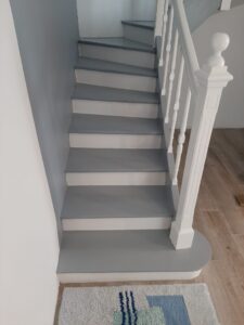 Escalier intérieur moderne avec marches grises, contremarches blanches et rampe blanche. Un tapis clair à motifs bleus est au sol.