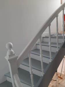 Rénovation d'escalier: marches grises, contremarches et balustrade blanches. Mur clair lumineux dans une maison moderne.