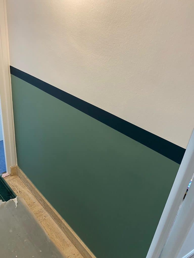 Mur bicolore avec peinture vert foncé et blanc cassé, séparé par une bande diagonale bleu marine. Décoration intérieure moderne.