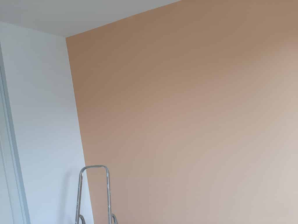 Peinture de chambre: un mur beige clair contrastant avec le blanc du plafond et d'un mur adjacent. Une échelle métallique est posée.